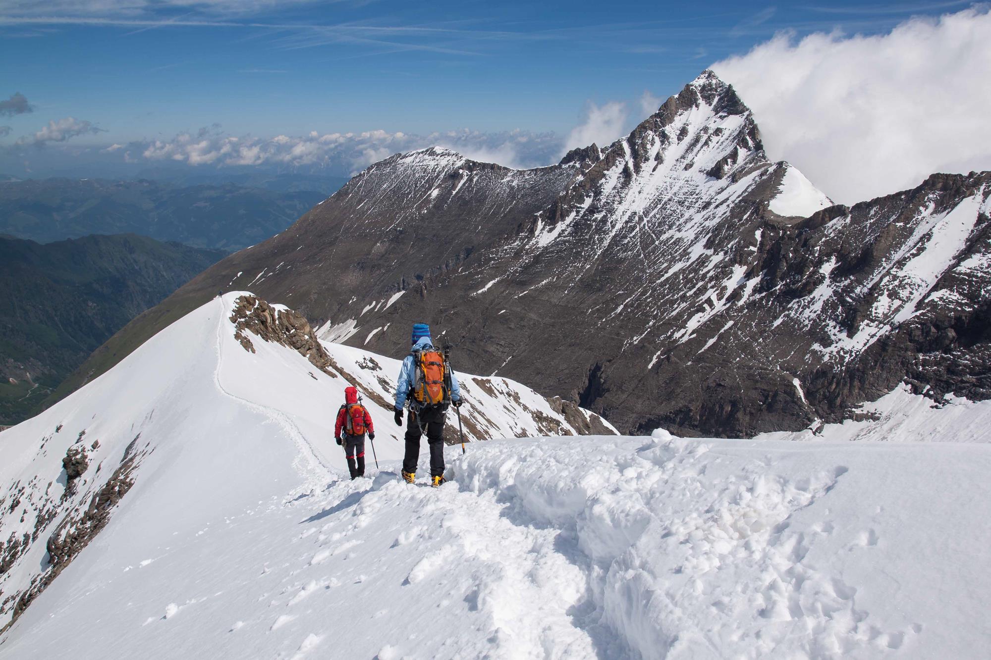 Zwei Bergsteigern gehen hintereinander auf einem verschneiten Grat.