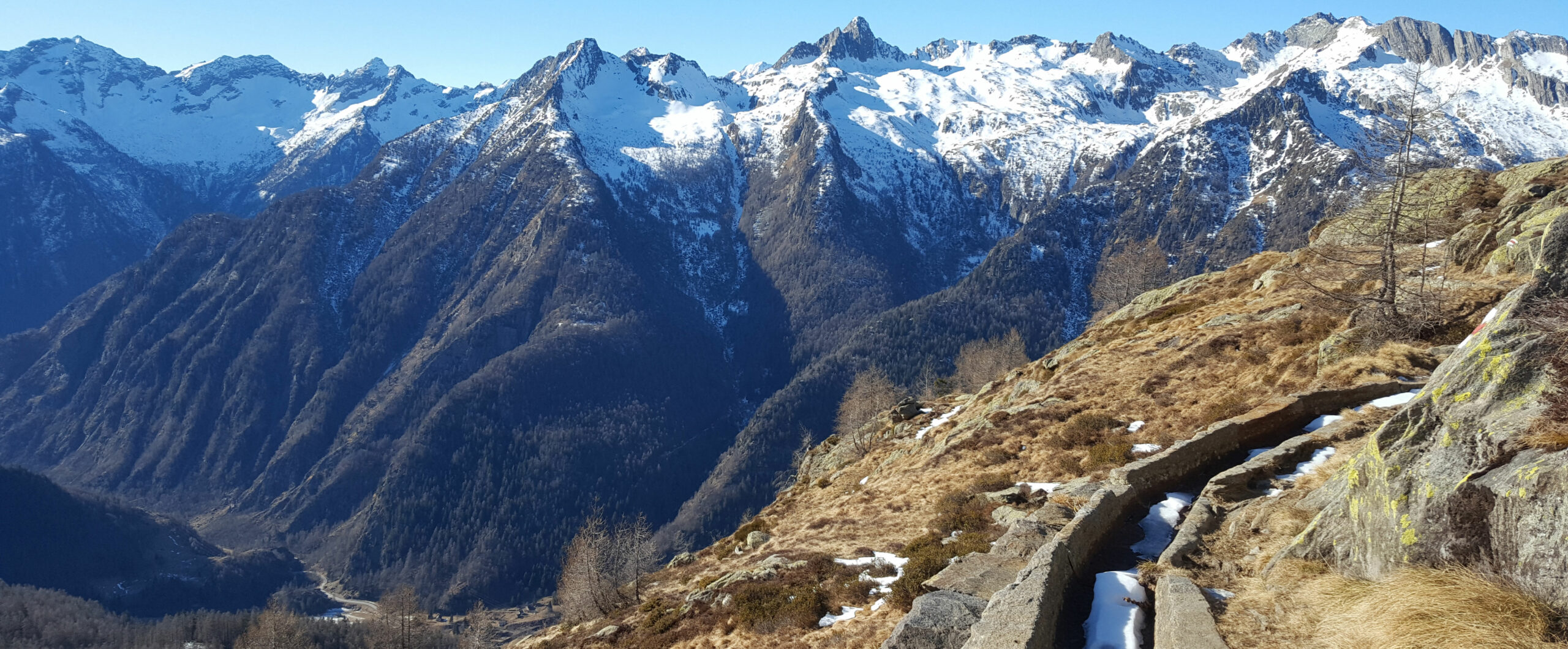 Ein Bergweg auf 2100 Meter im Februar fast schneefrei bei strahlendem Himmel mit hohen Bergen im Hintergrund