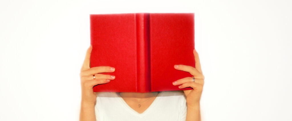 Eine Frau hält sich mit beiden Händen ein knallrotes Buch vor das Gesicht und liest darin