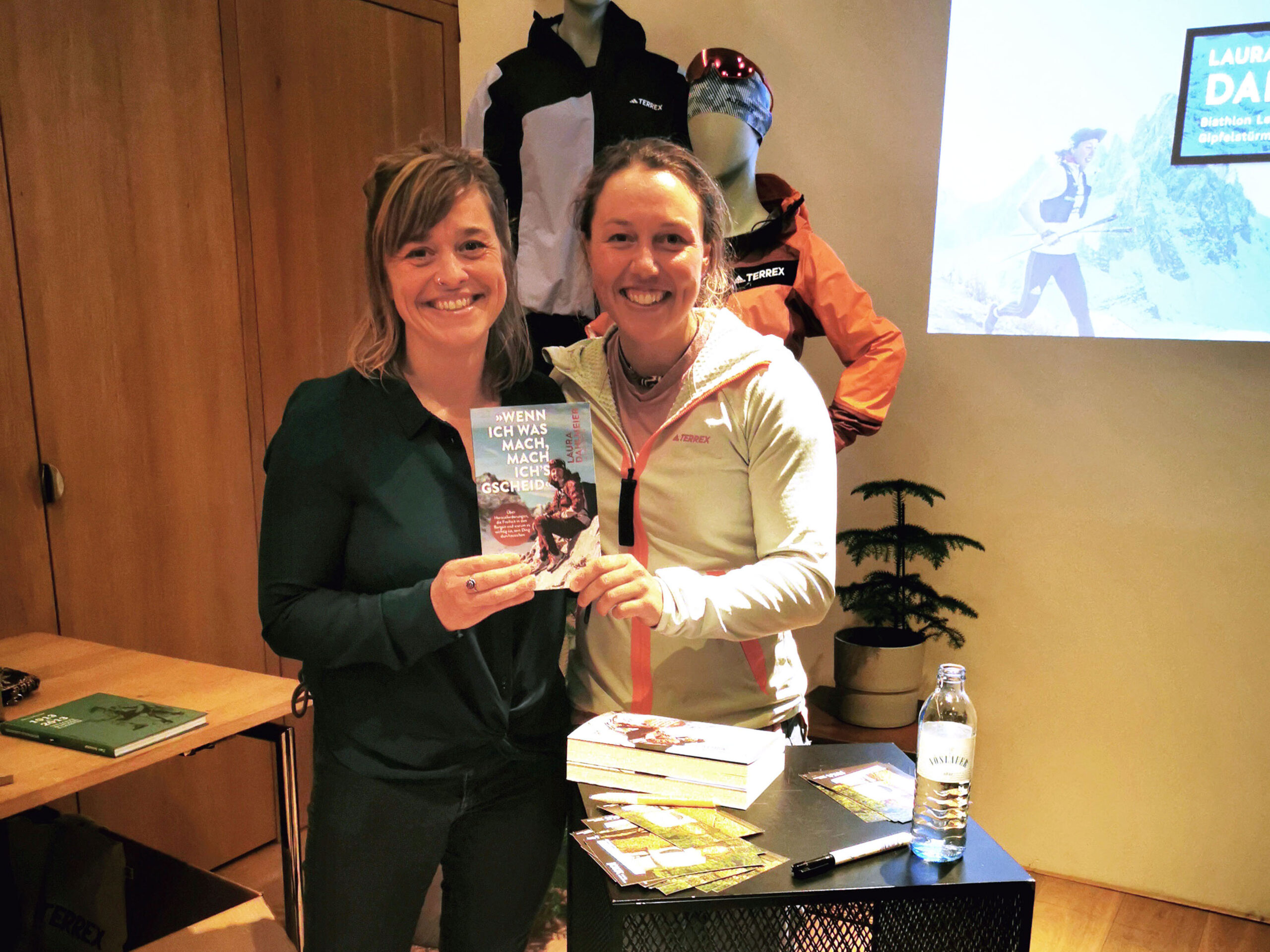 Biathlon-Olympiasiegerin Laura Dahlmeier und ihre Co-Autorin Franziska Kucera halten bei einer Buchvorstellung im Sporthaus Schuster strahlend ihr neues Buch in die Kamera.