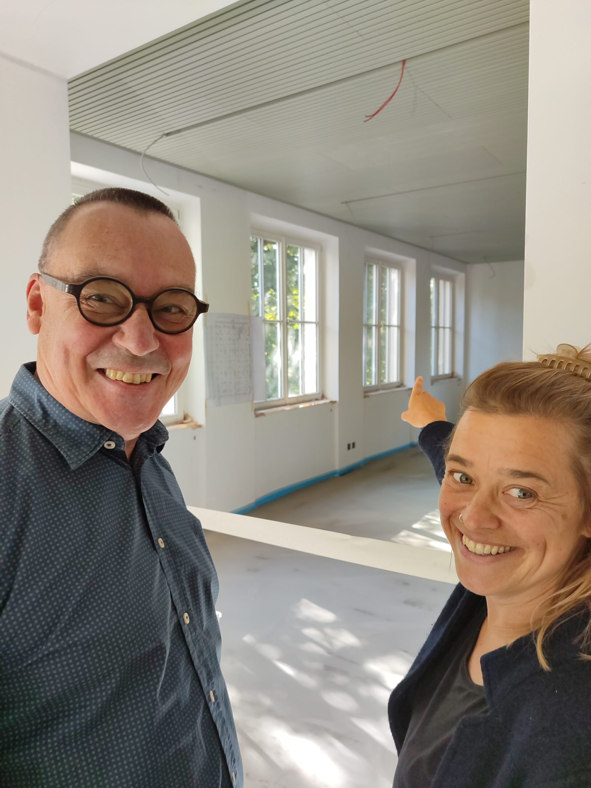 Frank Martin Siefarth und Franziska Kučera vom Medienbüro DiE WORTSTATT stehen vor einem leeren, noch in Renovierung befindlichen Raum im Alpinen Museum und lachen in die Kamera.